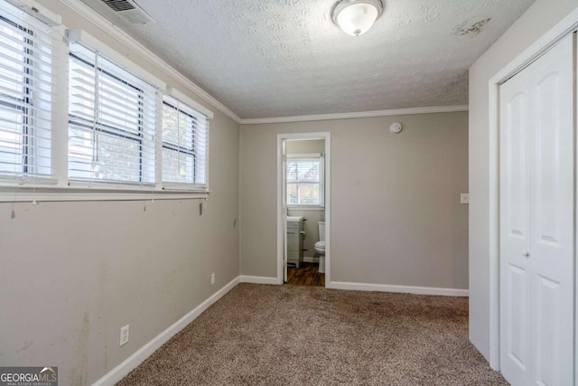 unfurnished bedroom featuring ensuite bath, ornamental molding, a textured ceiling, carpet floors, and a closet