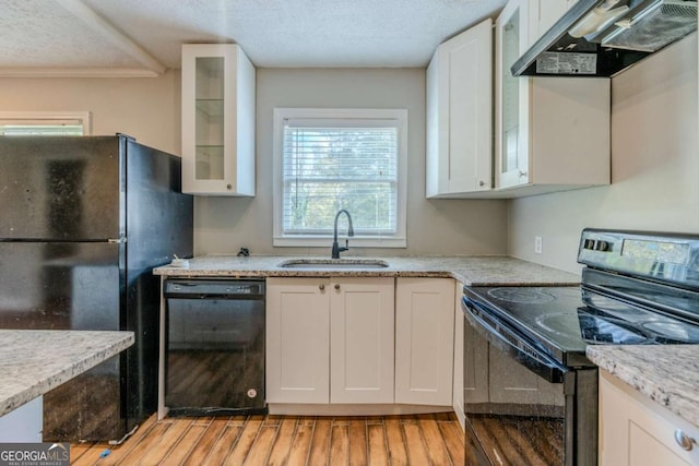 kitchen featuring sink, range hood, light hardwood / wood-style floors, white cabinets, and black appliances