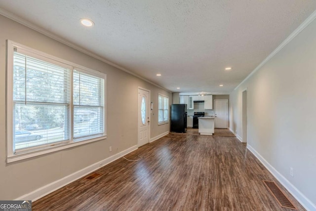 unfurnished living room featuring dark hardwood / wood-style flooring, ornamental molding, a textured ceiling, and a wealth of natural light