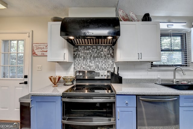 kitchen featuring appliances with stainless steel finishes, tasteful backsplash, wall chimney exhaust hood, sink, and white cabinets