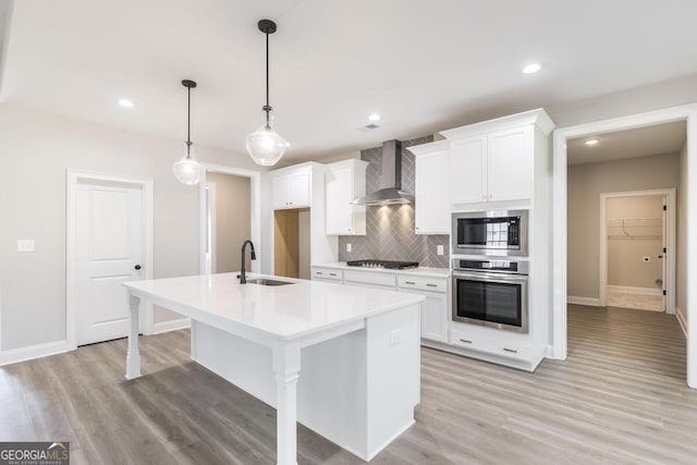 408 Bella Notte Cir Unit 26A, Warner Robins, GA 31088 - kitchen featuring appliances with stainless steel finishes, wall chimney range hood, tasteful backsplash, a kitchen island with sink, and light wood-type flooring