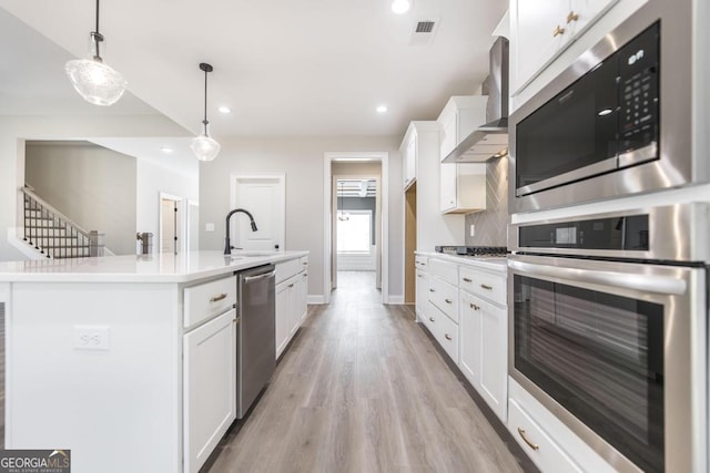 408 Bella Notte Cir Unit 26A, Warner Robins, GA 31088 - kitchen with appliances with stainless steel finishes, wall chimney exhaust hood, white cabinetry, light wood-type flooring, and decorative light fixtures