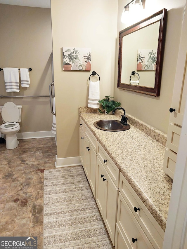bathroom with stone finish floor, vanity, toilet, and baseboards