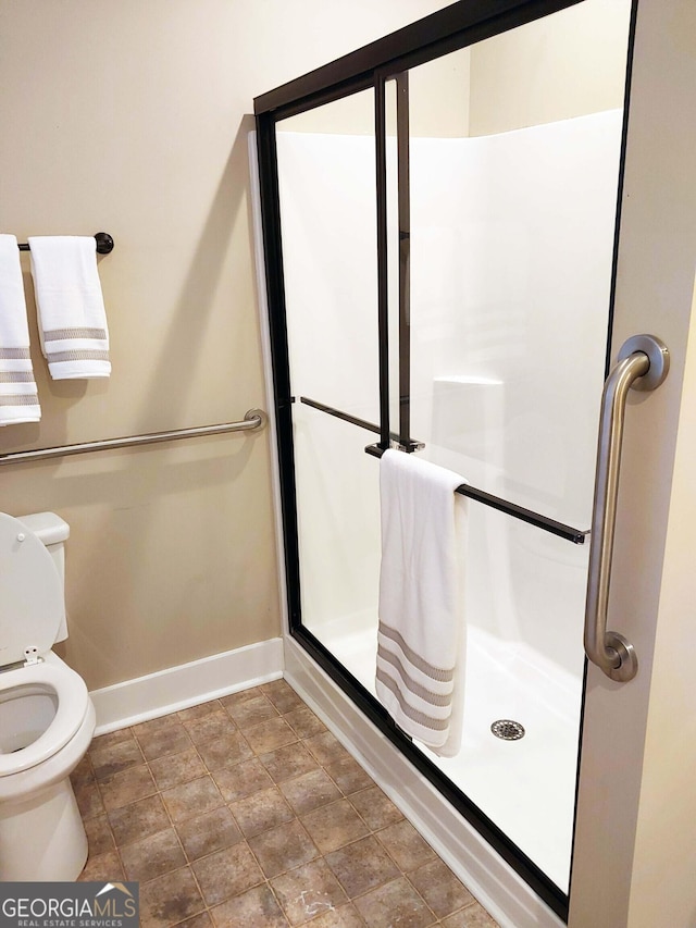 bathroom featuring a shower stall, baseboards, toilet, and stone finish floor