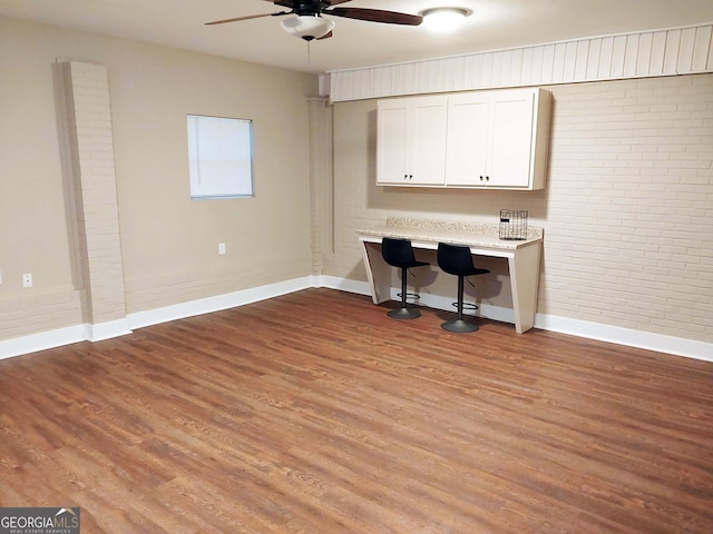 home office with brick wall, ceiling fan, baseboards, and wood finished floors