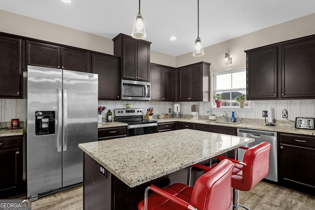 kitchen featuring pendant lighting, sink, appliances with stainless steel finishes, a kitchen island, and a breakfast bar area