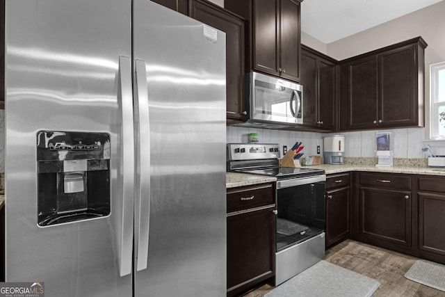 kitchen featuring dark brown cabinetry, light wood-type flooring, backsplash, and appliances with stainless steel finishes