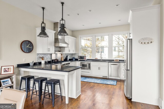 kitchen with kitchen peninsula, a kitchen bar, stainless steel appliances, decorative light fixtures, and white cabinetry