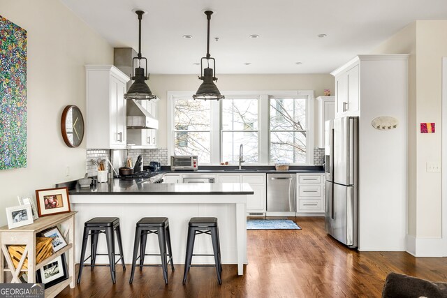 kitchen featuring white cabinets, a kitchen breakfast bar, decorative light fixtures, kitchen peninsula, and stainless steel appliances