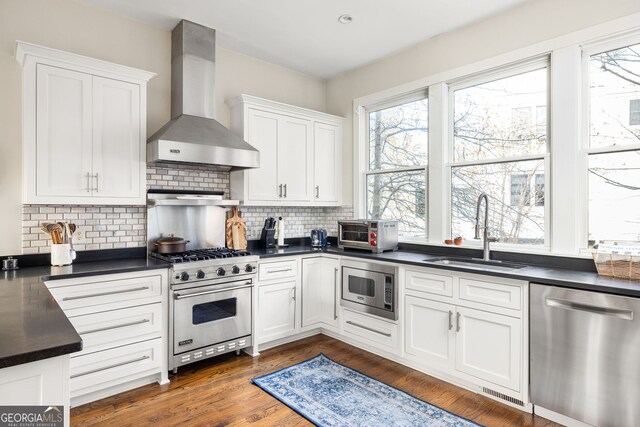 kitchen with tasteful backsplash, stainless steel appliances, sink, wall chimney range hood, and white cabinetry