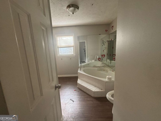 bathroom featuring hardwood / wood-style floors, a relaxing tiled tub, a textured ceiling, and toilet