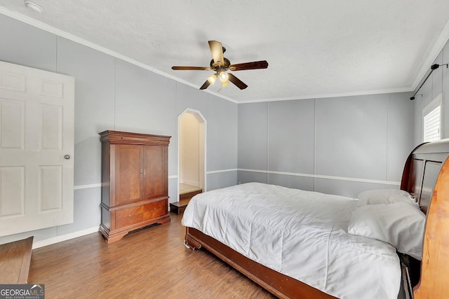 bedroom with a textured ceiling, ceiling fan, wood-type flooring, and crown molding