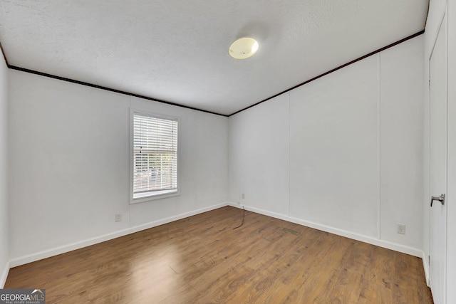 empty room featuring hardwood / wood-style floors, ornamental molding, and a textured ceiling