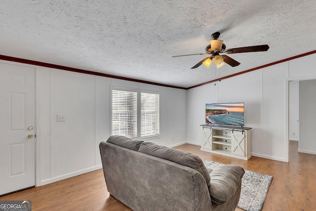 living room with a textured ceiling, ceiling fan, light wood-type flooring, and ornamental molding