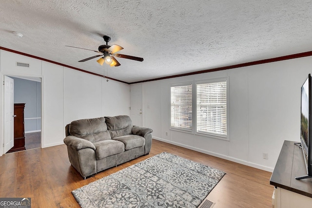 living room with wood-type flooring, a textured ceiling, ceiling fan, and ornamental molding