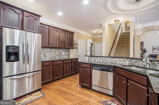 kitchen with light wood-type flooring, stainless steel appliances, sink, dark stone countertops, and hanging light fixtures