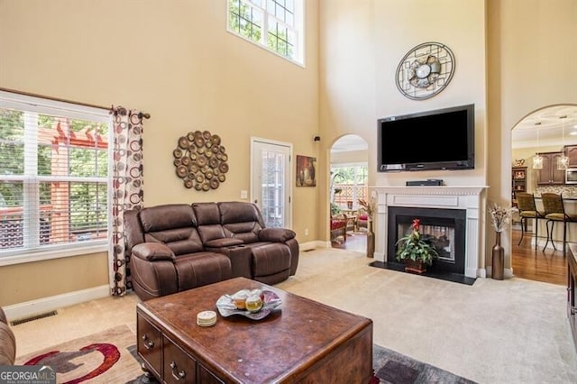 carpeted living room featuring a multi sided fireplace, a towering ceiling, and a healthy amount of sunlight