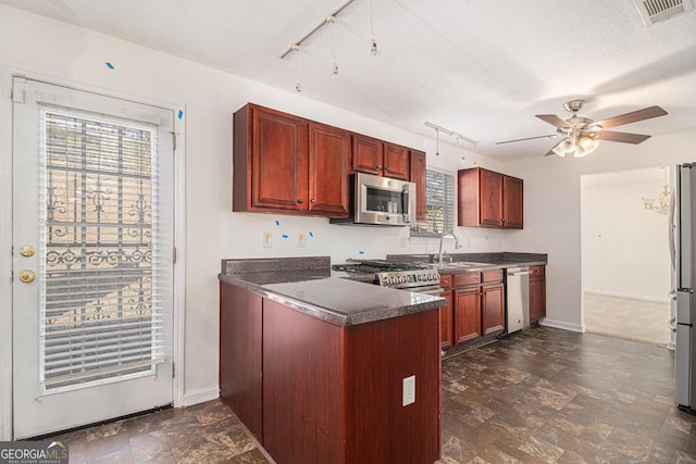 kitchen featuring stainless steel appliances, a peninsula, a sink, dark brown cabinets, and dark countertops