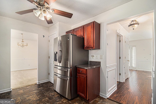 kitchen featuring baseboards, dark countertops, a textured ceiling, stainless steel refrigerator with ice dispenser, and ceiling fan with notable chandelier