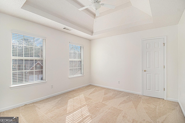 spare room with ceiling fan, a textured ceiling, light colored carpet, baseboards, and a raised ceiling