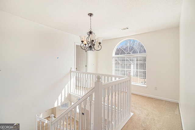 corridor with a chandelier, an upstairs landing, visible vents, baseboards, and carpet