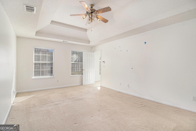 spare room featuring a textured ceiling, light carpet, visible vents, baseboards, and a raised ceiling