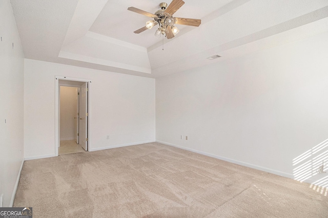 spare room with baseboards, ceiling fan, a raised ceiling, and light colored carpet