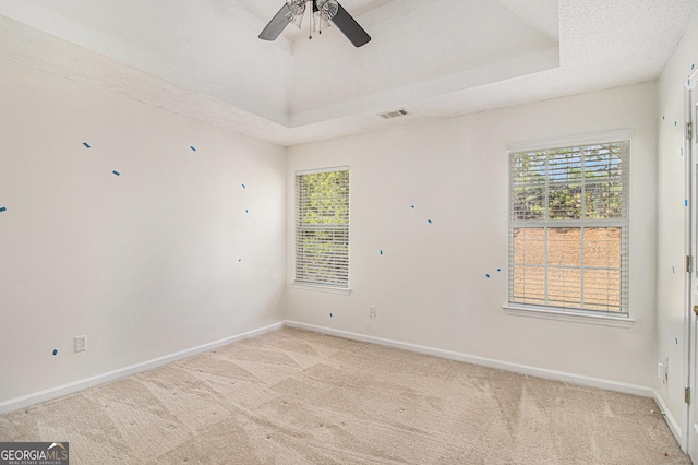 unfurnished room with light carpet, a tray ceiling, visible vents, and baseboards