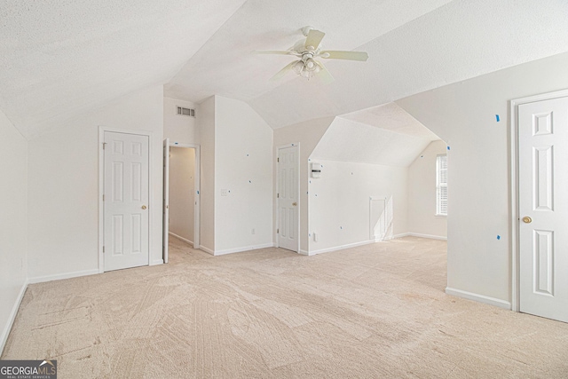 additional living space with a textured ceiling, vaulted ceiling, visible vents, and light colored carpet