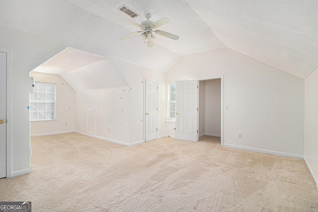 additional living space with a textured ceiling, vaulted ceiling, carpet flooring, and visible vents