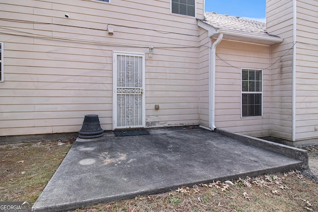 property entrance with a shingled roof and a patio area