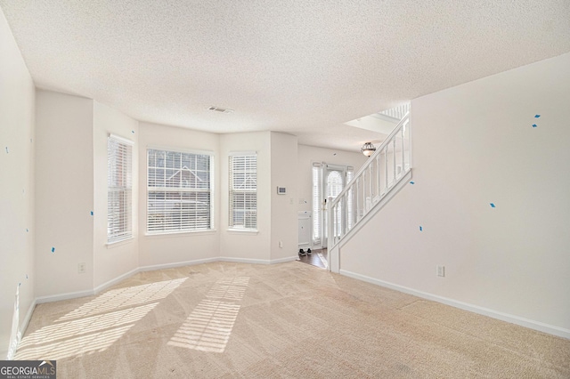 empty room featuring light carpet, baseboards, stairway, and a textured ceiling