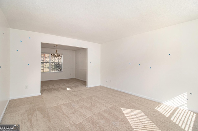 spare room with a chandelier, a textured ceiling, baseboards, and light colored carpet