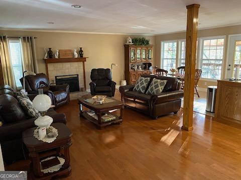 living room with a tiled fireplace, wood-type flooring, a wealth of natural light, and ornate columns