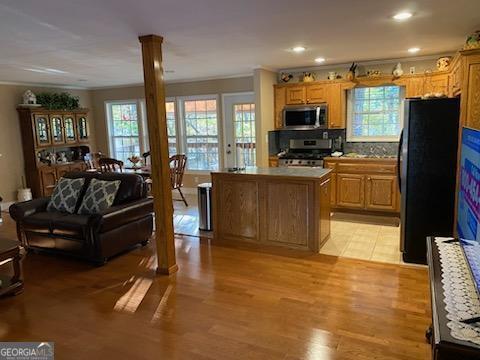 kitchen with appliances with stainless steel finishes, decorative columns, a center island, light hardwood / wood-style floors, and decorative backsplash