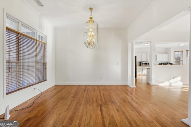 spare room with a chandelier, light hardwood / wood-style flooring, crown molding, and ornate columns