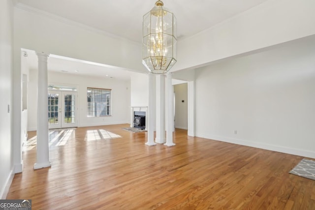 unfurnished living room featuring french doors, decorative columns, hardwood / wood-style floors, a chandelier, and ornamental molding