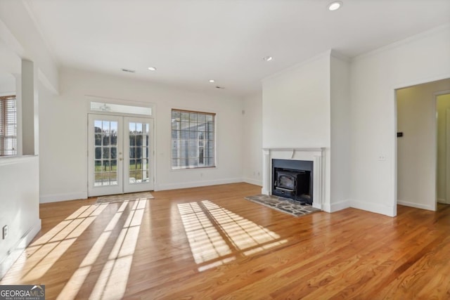 unfurnished living room with french doors, light hardwood / wood-style floors, a wood stove, and ornamental molding