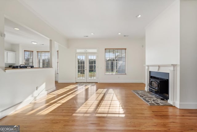 unfurnished living room featuring a wood stove, french doors, crown molding, and light hardwood / wood-style flooring