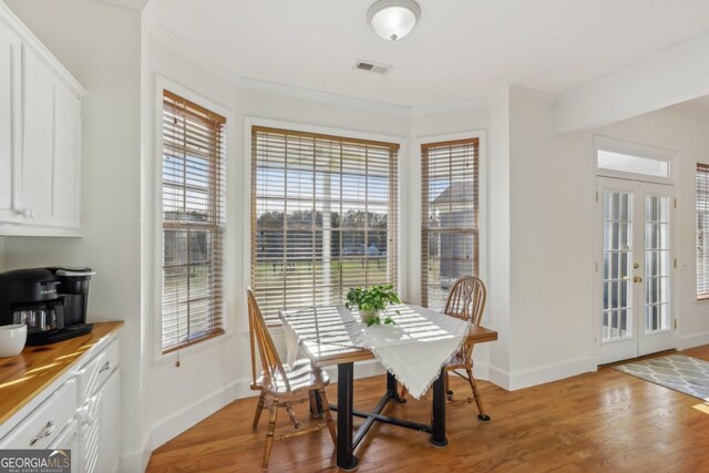 dining area with french doors, light wood-type flooring, and ornamental molding