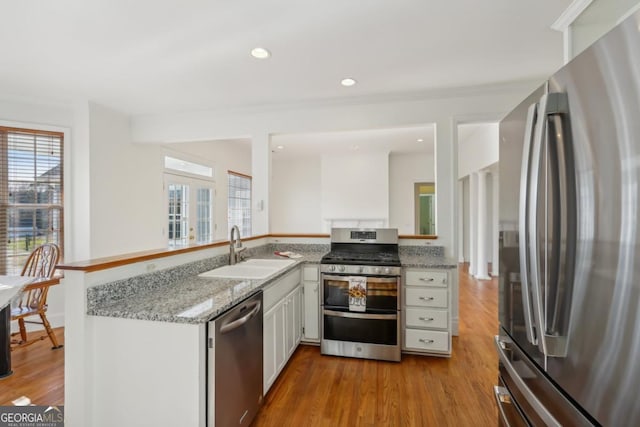 kitchen with kitchen peninsula, appliances with stainless steel finishes, light wood-type flooring, sink, and white cabinetry