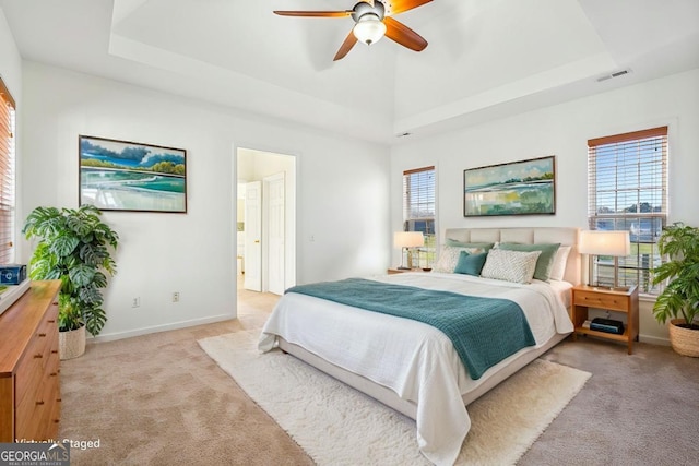 bedroom with a tray ceiling, ensuite bathroom, ceiling fan, and light carpet