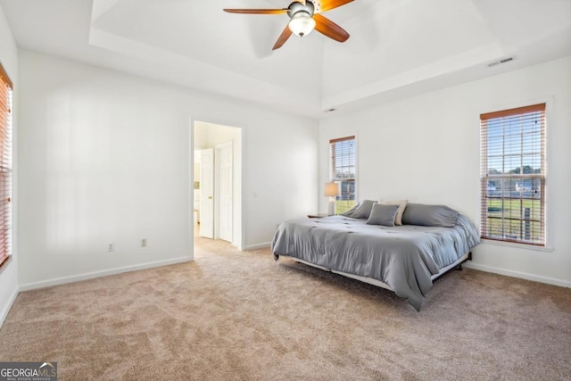 bedroom featuring a tray ceiling, ceiling fan, ensuite bathroom, and light carpet