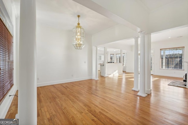 unfurnished living room with ornate columns, light wood-type flooring, and an inviting chandelier