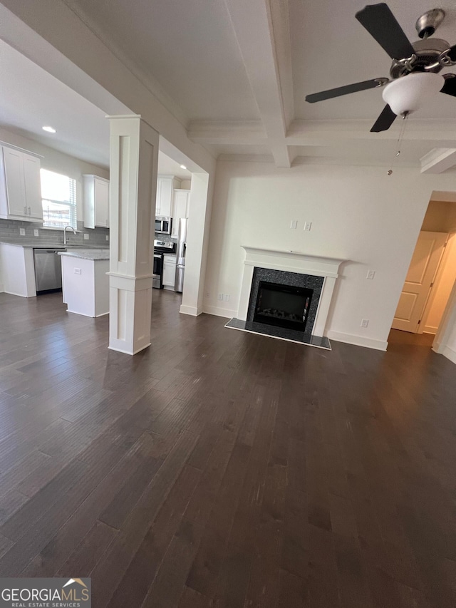 unfurnished living room featuring ceiling fan, sink, beamed ceiling, a high end fireplace, and dark hardwood / wood-style floors