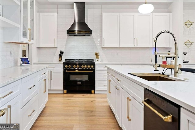 kitchen with decorative light fixtures, sink, white cabinets, black appliances, and wall chimney exhaust hood