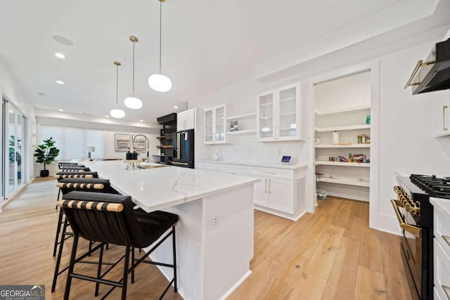 kitchen with high quality appliances, white cabinets, a kitchen bar, a kitchen island with sink, and light stone countertops