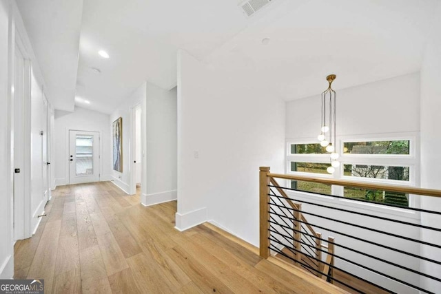 hall featuring vaulted ceiling, light hardwood / wood-style floors, and a chandelier