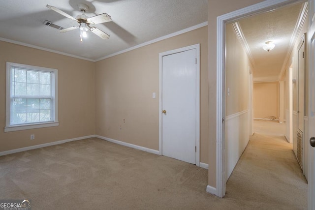 spare room featuring light carpet, a textured ceiling, ceiling fan, and ornamental molding