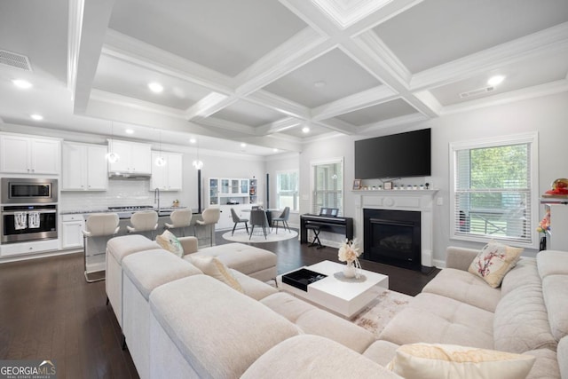 living room featuring beamed ceiling, dark wood-type flooring, coffered ceiling, and ornamental molding